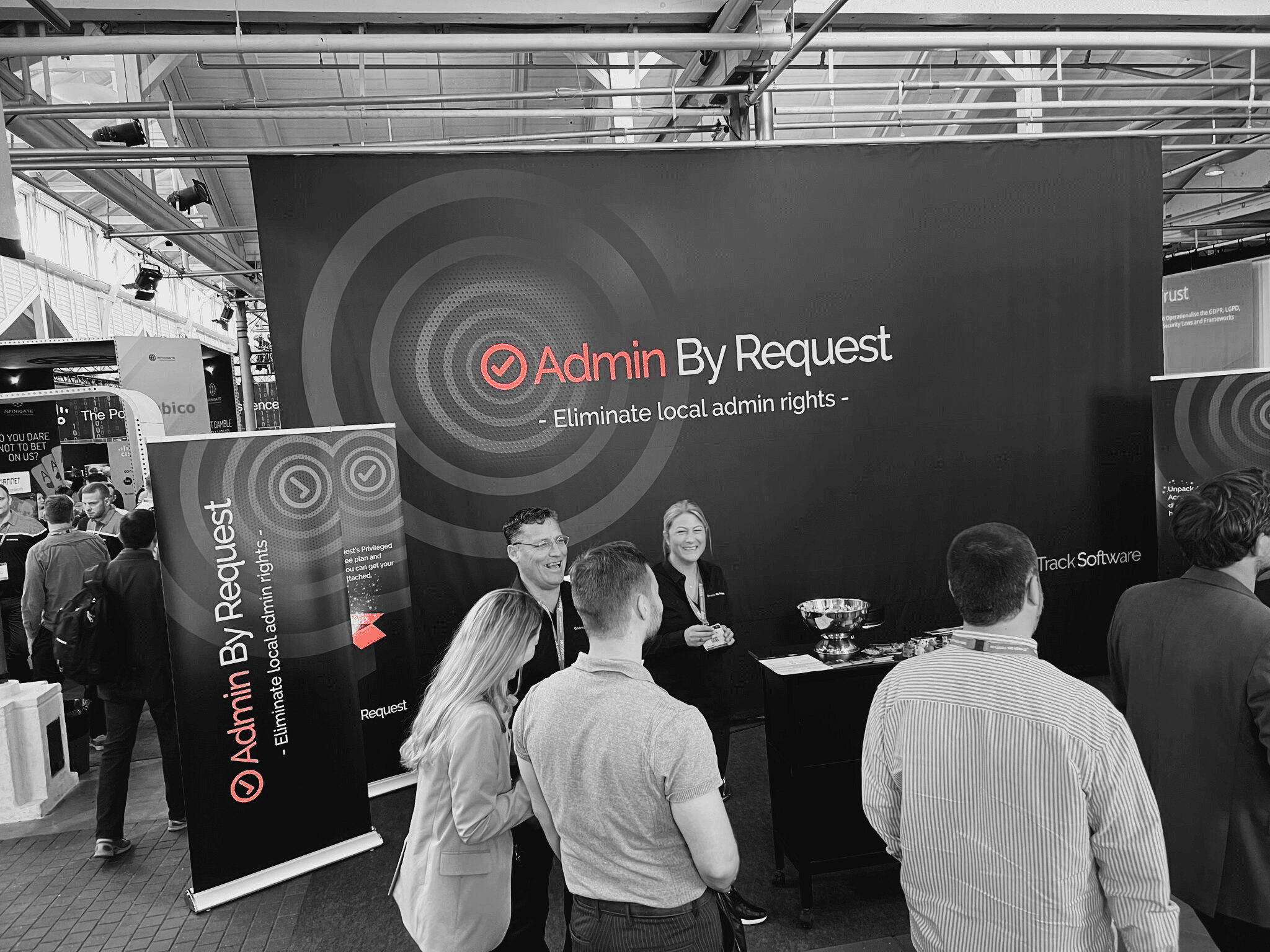 A black, white and orange image of some people laughing at an admin by request conference. » admin by request