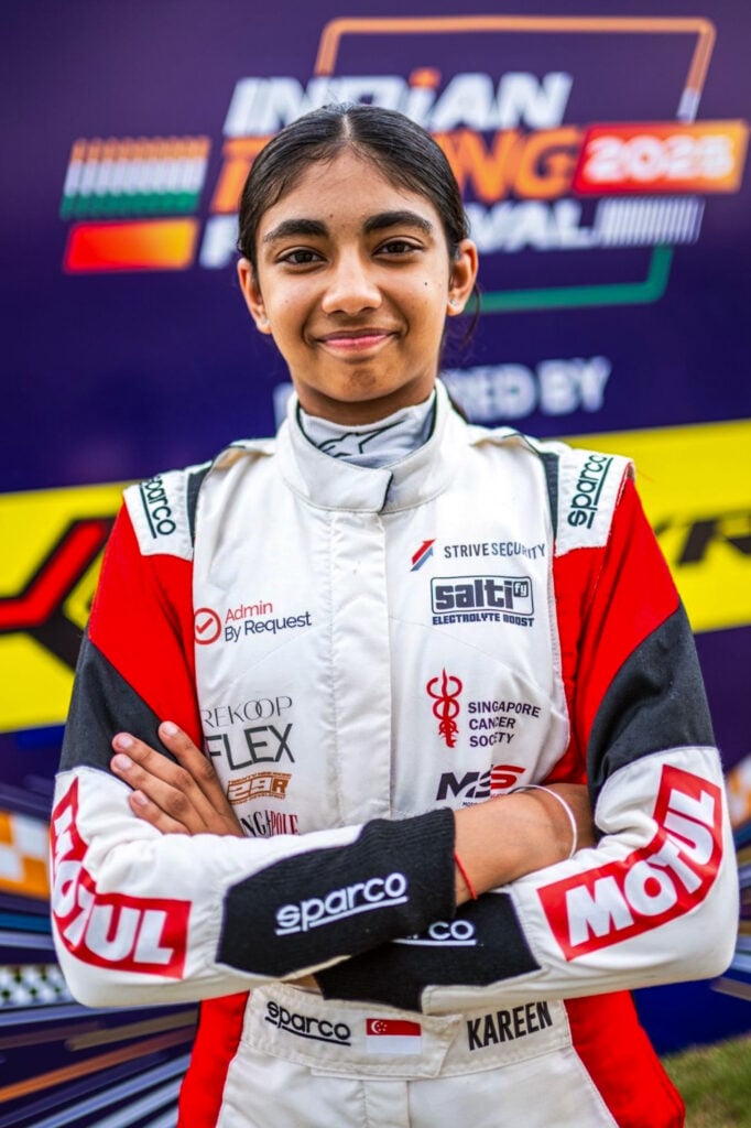 Portrait of a young race car driver in a white and red sparco racing suit, arms crossed, smiling in front of a purple sponsor banner; belt reads kareem with a singapore flag. » admin by request