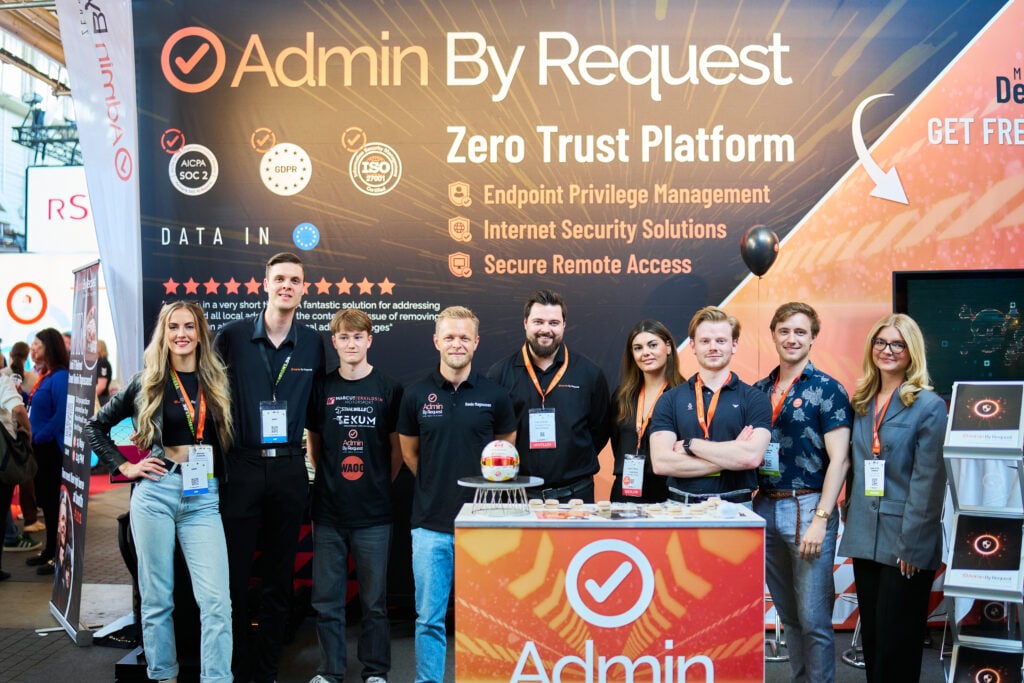 Group of smiling people at an expo booth with large ‘admin by request’ banner in the background. » admin by request