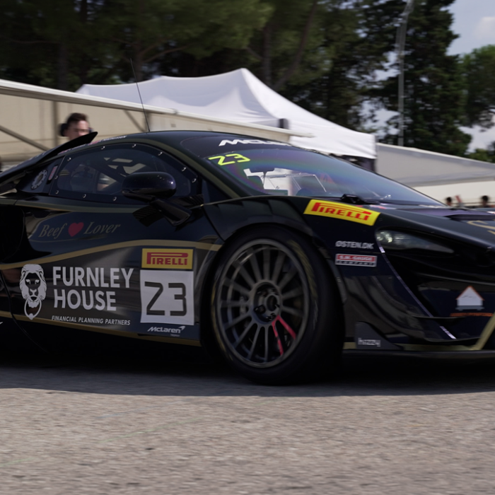 Black race car with number 23 and sponsor logos in a paddock area under white tents, rear wing visible behind the vehicle. » admin by request