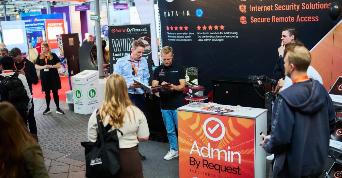 Exhibition booth for Admin By Request with staff showing materials at a tech trade show.