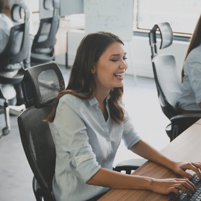 A happy woman on her computer with four of her co-workers in the background of the office. » admin by request