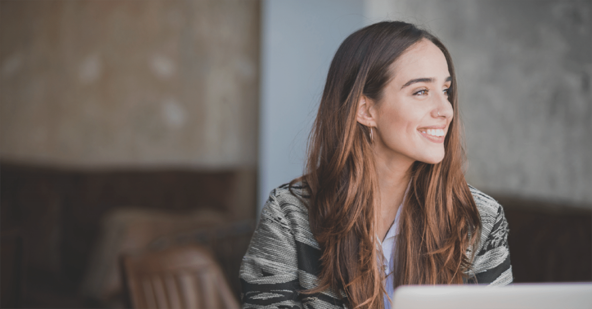 A woman who is sitting at her computer desk smiling to the right side.