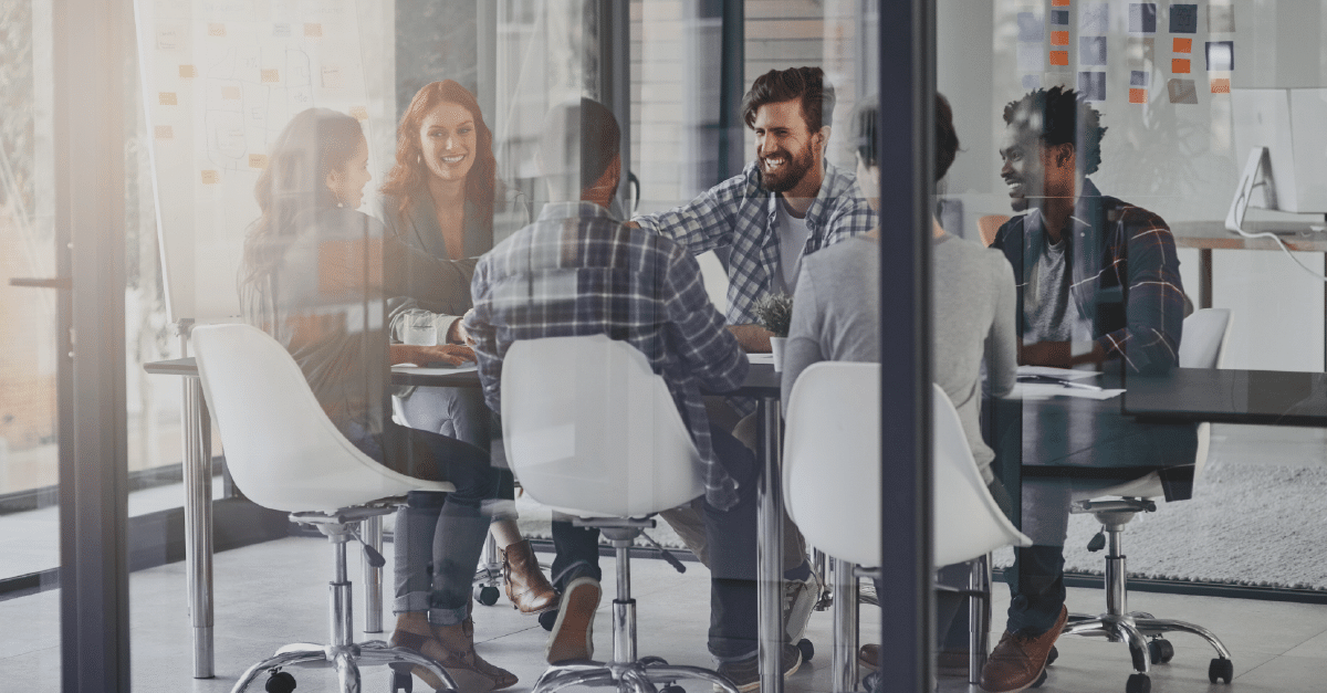 A photo through glass walls of six people in a meeting enjoying themselves.